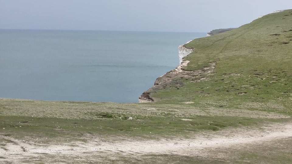 Seven Sisters 的短草坡从鞍部向下一段山脊抬升，左侧白垩崖面露在海面上方。