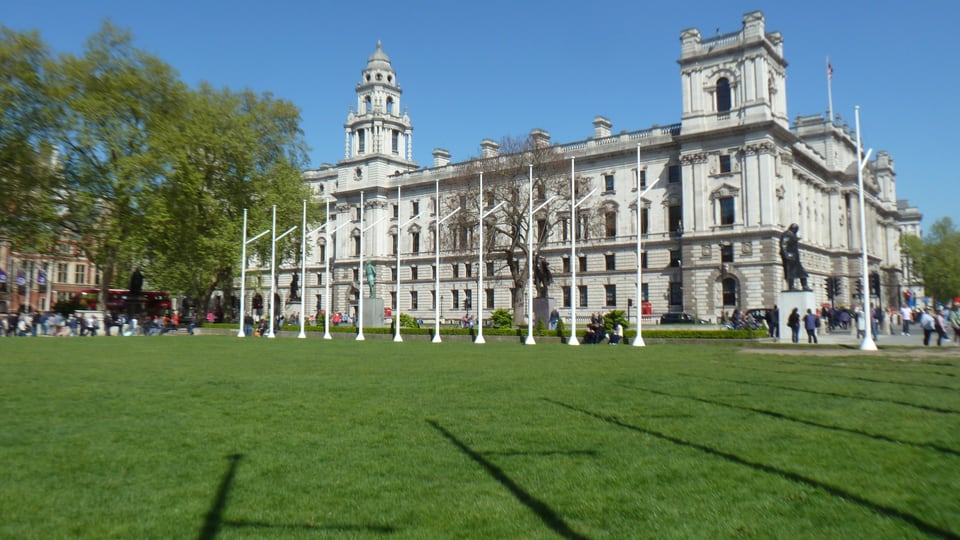 Parliament Square 的草地、雕像与旗杆排在前景，HM Treasury 的浅色立面沿广场北侧展开。