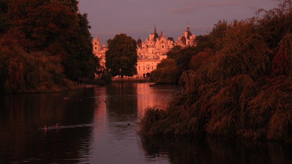 St James’s Park 湖面映着橙红暮色，远处树木与建筑轮廓围住水岸。