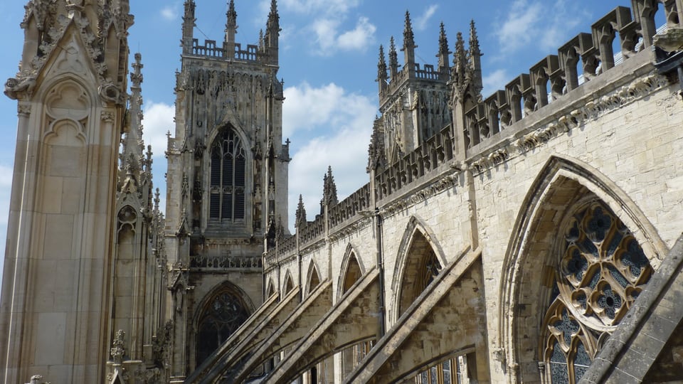 York Minster 的西塔与哥特式飞扶壁在蓝天下沿中殿延伸。