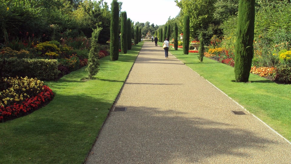 Regent's Park 的 Avenue Gardens 沿中轴延伸，修剪绿篱、柱形树木、花坛与远处喷泉分列步道两侧。